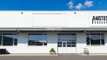 Moderne Gewerbefassade mit großen Fenstern und einem Sektionaltor, umgeben von einem gepflegten Außenbereich.