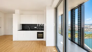 Moderne Küche mit weißen Schränken, dunkler Arbeitsplatte und Zugang zu einem Balkon mit Stadt- und Seeblick.