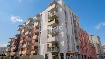 Modernes Mehrfamilienhaus mit zahlreichen Balkonen und Geschäften im Erdgeschoss.
