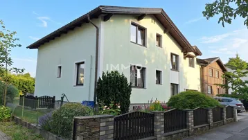 Gepflegte Hausfassade mit Vorgarten und Zaun bei sonnigem Wetter.