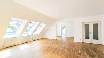 Helles Dachgeschoss-Wohnzimmer mit Holzboden und mehreren Dachfenstern für viel Tageslicht.