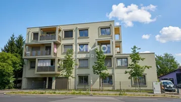 Modernes Mehrfamilienhaus mit mehreren Balkonen und großen Fenstern in städtischer Umgebung.