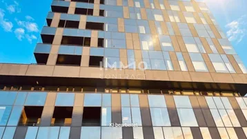 Moderne Gebäudefassade mit Glas- und Betonelementen unter blauem Himmel, die das Sonnenlicht reflektiert.
