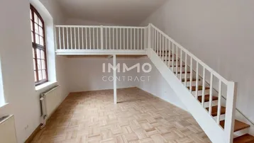 Heller Wohnraum mit Parkettboden und einer Holztreppe, die zu einer Galerie führt.