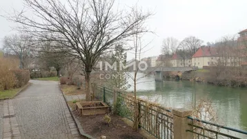Blick auf den Fluss mit einer Brücke und Bäumen am Ufer an einem bewölkten Tag.