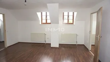 Helles Zimmer im Dachgeschoss mit Laminatboden, weißen Wänden und zwei Dachgaubenfenstern.