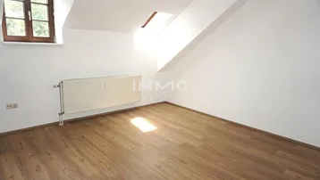 Helles Zimmer im Dachgeschoss mit Laminatboden, Dachfenster und Heizkörper.