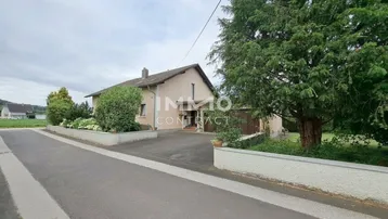 Das Haus präsentiert sich mit einer gepflegten Fassade, einer Einfahrt und umgebendem Grün in ländlicher Umgebung.