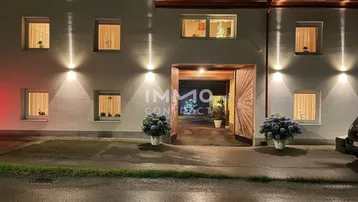Beleuchtete Fassade eines Wohnhauses bei Nacht mit einladendem Eingangsbereich und dekorativen Pflanzen.