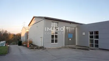 Außenansicht eines Industriegebäudes mit Wellblechfassade und großem Einfahrtstor, umgeben von einer Zufahrt.