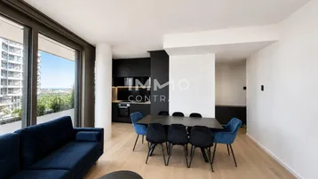 Moderner offener Wohn- und Essbereich mit Holzboden, blauer Couch und integrierter schwarzer Küche.