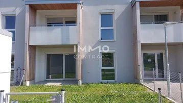 Moderne Reihenhäuser mit Balkonen und kleinen Gärten, umgeben von einer grünen Umgebung.