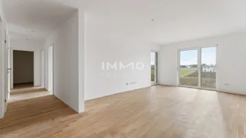 Geräumiger, heller Wohnbereich mit Holzboden und großen Fenstern mit Blick ins Grüne.