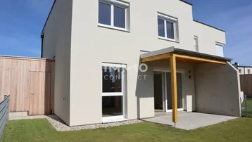 Rückseite eines modernen Reihenhauses mit kleiner Rasenfläche und überdachter Terrasse.