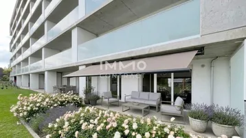 Moderne Erdgeschosswohnung mit großer möblierter Terrasse, umgeben von blühenden Rosenbeeten und Rasenfläche.