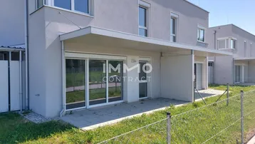Moderne Reihenhausfassade mit kleiner gepflasterter Terrasse und Zugang zum Gartenbereich.