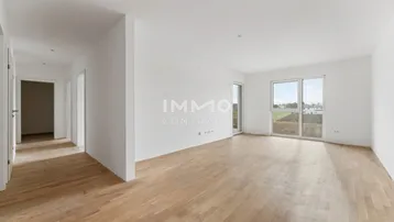 Leerer Raum mit hellem Parkettboden, großen Fenstern und weitem Blick ins Grüne.