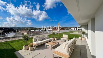 Geräumige Dachterrasse mit moderner Lounge-Möblierung, Rasenfläche und weitem Blick auf die umliegende Landschaft und Berge.