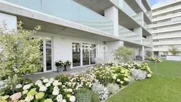 Moderne Erdgeschosswohnung mit privatem Garten, blühenden Blumenbeeten und einer möblierten Terrasse.