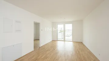 Geräumiges Wohnzimmer mit Holzboden, weißen Wänden und Zugang zu einem französischen Balkon.