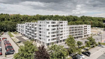 Luftaufnahme eines modernen Wohnkomplexes mit mehreren Gebäuden, Balkonen und umliegenden Parkplätzen.