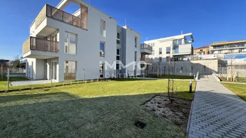 Modernes Apartmentgebäude mit Balkonen, gepflegtem Rasen und Gehwegen unter blauem Himmel.