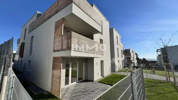 Modernes Mehrfamilienhaus mit heller Fassade, Holzdetails an Balkonen und gepflegter Grünfläche.