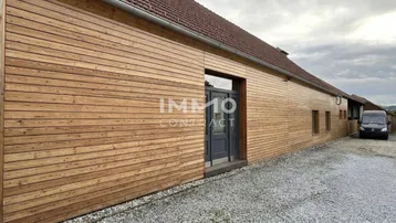 Gebäudeaußenansicht mit moderner Holzfassade und dunkler Eingangstür, umgeben von einem Kiesweg.