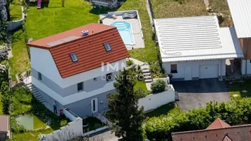 Luftaufnahme eines modernen Einfamilienhauses mit Garten, Pool, Spielplatz und Garage.