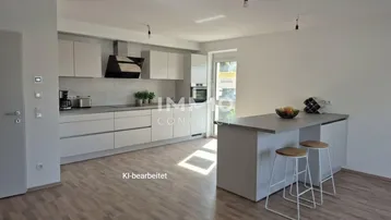 Moderne offene Küche mit Kücheninsel, hellgrauen Schränken und Laminatboden in einem Wohnraum.