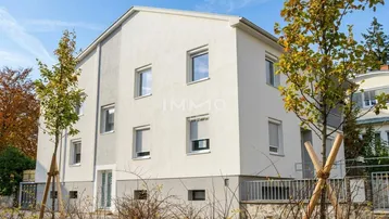 Modernes Mehrfamilienhaus mit heller Fassade und großen Fenstern, umgeben von jungen Bäumen.