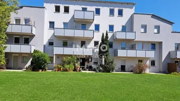 Mehrfamilienhaus mit Balkonen, Terrassen und einer gepflegten Grünfläche im Vordergrund.