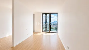 Helles, leeres Zimmer mit Holzboden und großen Fenstern, die einen weiten Blick auf die Stadt und das Wasser bieten.