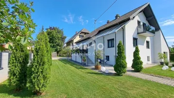 Weißes Einfamilienhaus mit gepflegtem Rasen und modernem Anbau unter blauem Himmel.
