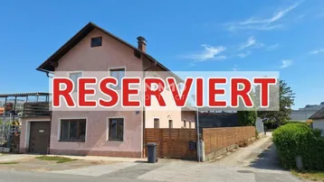 Außenansicht eines gepflegten Wohnhauses mit Satteldach, Garage und Holzzaun unter blauem Himmel.
