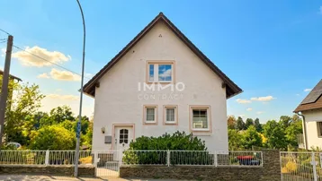 Gepflegtes weißes Einfamilienhaus mit Satteldach, kleinem Vorgarten und Zaun unter blauem Himmel.