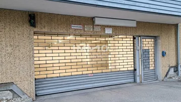 Einfahrt zu einer Tiefgarage mit geschlossenem Rolltor, separater Zugangstür und blauer Fassadenverkleidung.