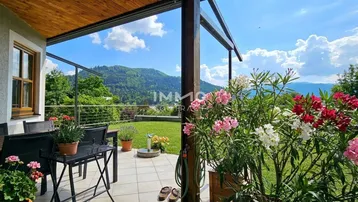 Gemütliche Terrasse mit Gartenmöbeln, blühenden Pflanzen und weitem Bergblick.
