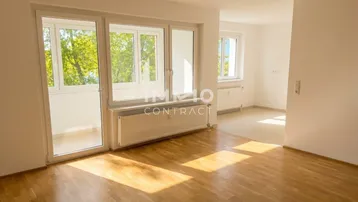 Helles Zimmer mit Parkettboden, großen Fenstern und Zugang zu einem Balkon, ideal als Wohnbereich.