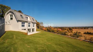 Modernes Haus mit Mansarddach und großem Rasen auf einem Hügel mit weitem Blick über die Landschaft.