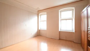 Helles Zimmer mit Laminatboden, zwei Fenstern und einer Decke mit Stuckverzierungen.