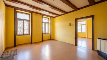 Geräumiges Zimmer mit gelben Wänden, Holzbalkendecke und Laminatboden, bereit zur Renovierung.