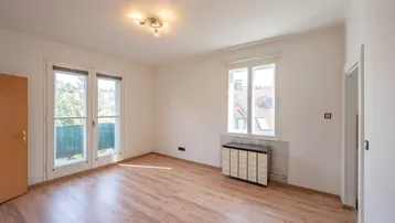 Helles Zimmer mit Laminatboden, Balkonzugang und einem Fenster mit Blick nach draußen.
