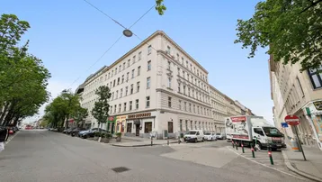 Historisches Gebäude an einer belebten Straße mit Bäumen und parkenden Autos.