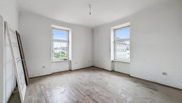 Helles, unmöbliertes Zimmer mit zwei Fenstern und altem Parkettboden, bereit zur Renovierung.