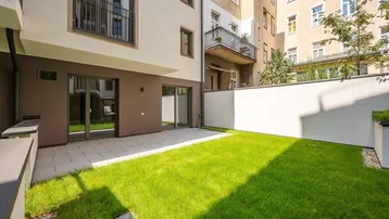 Gepflasterte Terrasse und Rasenfläche im Innenhof eines modernen Wohngebäudes.