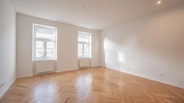 Helles, leeres Zimmer mit Fischgrätparkettboden und zwei großen Fenstern, ideal als Wohnzimmer.
