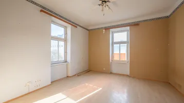 Helles Zimmer mit hellem Parkettboden, zwei Fenstern und einem Deckenventilator, bereit zur Renovierung.