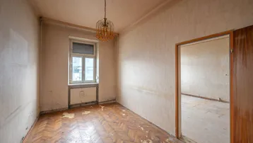 Leerer Raum mit altem Parkettboden, abgenutzter Tapete und einem Fenster, bereit zur Renovierung.