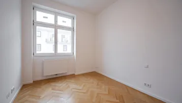 Helles Zimmer mit Fischgrätparkett und großem Fenster, bereit zur individuellen Gestaltung.